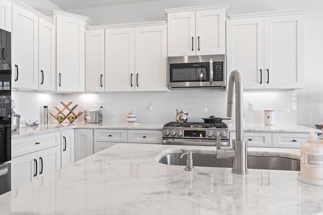 kitchen featuring tasteful backsplash, white cabinetry, appliances with stainless steel finishes, and light stone counters