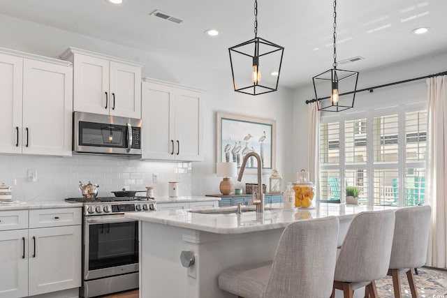 kitchen featuring hanging light fixtures, stainless steel appliances, white cabinets, and a center island with sink