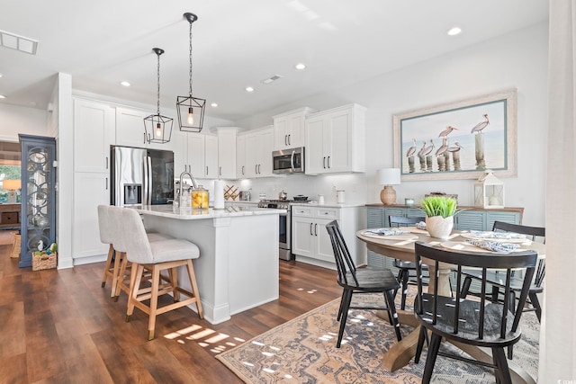 kitchen featuring stainless steel appliances, white cabinets, and a center island with sink