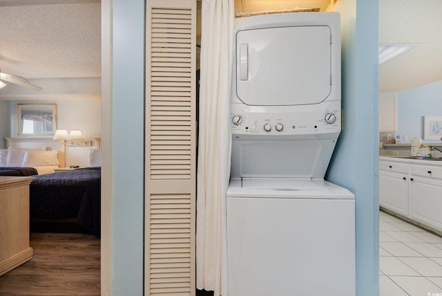 clothes washing area with stacked washer / dryer, sink, ceiling fan, light hardwood / wood-style floors, and a textured ceiling