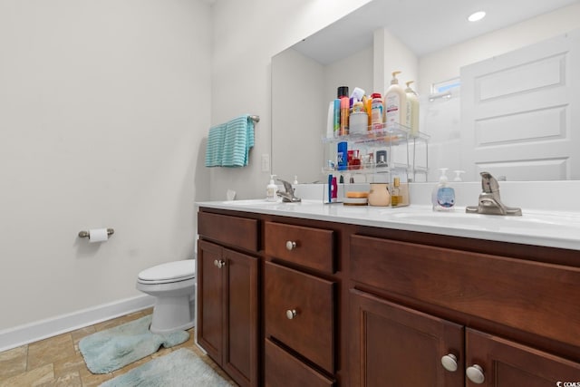 bathroom featuring double vanity, a sink, toilet, and baseboards