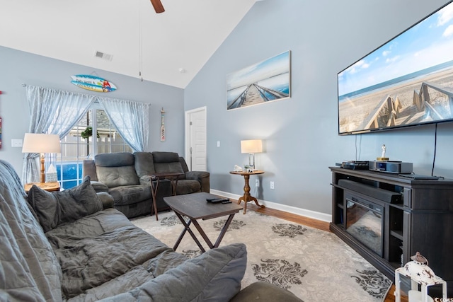 living area featuring ceiling fan, high vaulted ceiling, wood finished floors, visible vents, and baseboards