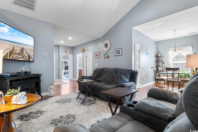 living room featuring a notable chandelier, lofted ceiling, visible vents, wood finished floors, and baseboards