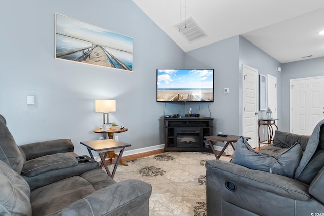 living area featuring visible vents, a glass covered fireplace, vaulted ceiling, wood finished floors, and baseboards