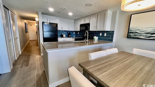 kitchen featuring tasteful backsplash, black appliances, sink, white cabinets, and kitchen peninsula