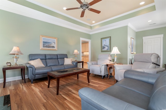 living room with hardwood / wood-style flooring, crown molding, a raised ceiling, and ceiling fan