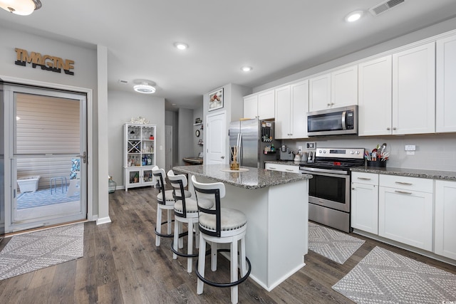 kitchen featuring white cabinetry, appliances with stainless steel finishes, a kitchen island, and dark stone counters