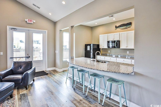 kitchen featuring sink, a breakfast bar, black appliances, light stone countertops, and white cabinets