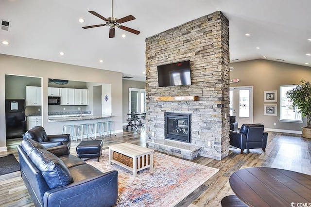 living room with a stone fireplace, sink, vaulted ceiling, light wood-type flooring, and ceiling fan