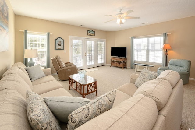 living area featuring baseboards, a healthy amount of sunlight, a ceiling fan, and light colored carpet