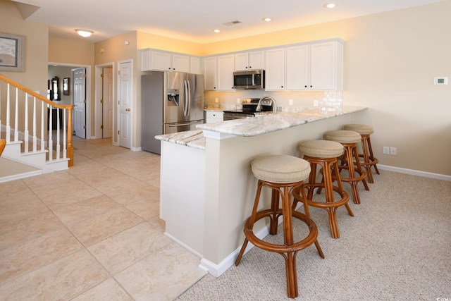 kitchen featuring light stone counters, stainless steel appliances, tasteful backsplash, white cabinetry, and a peninsula