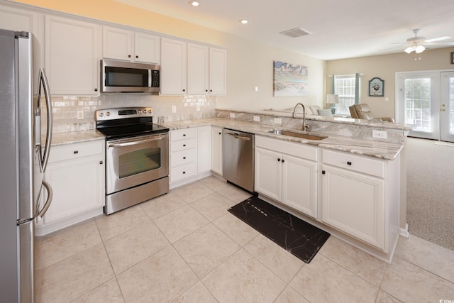 kitchen with sink, white cabinetry, appliances with stainless steel finishes, kitchen peninsula, and light stone countertops