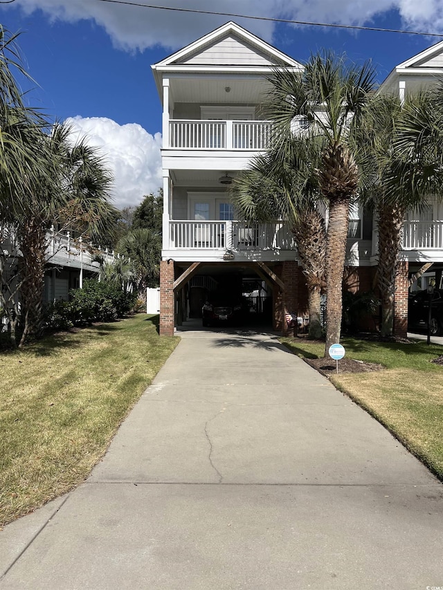 coastal inspired home with concrete driveway, covered porch, a balcony, a carport, and a front lawn