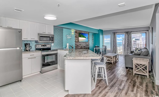 kitchen featuring white cabinets, a breakfast bar area, open floor plan, light stone countertops, and stainless steel appliances