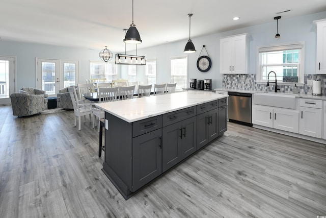 kitchen featuring decorative light fixtures, white cabinetry, dishwasher, sink, and a center island