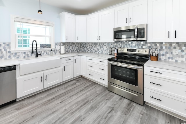 kitchen featuring sink, appliances with stainless steel finishes, white cabinetry, light hardwood / wood-style floors, and decorative light fixtures