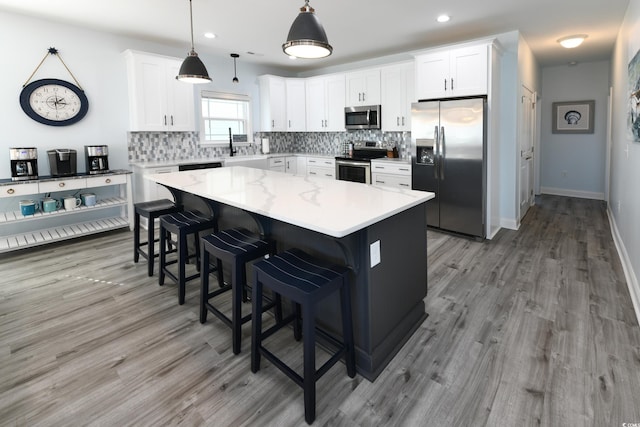 kitchen featuring pendant lighting, a kitchen island, white cabinets, and appliances with stainless steel finishes