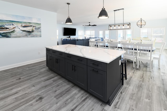 kitchen featuring a kitchen island, pendant lighting, light stone counters, and light hardwood / wood-style floors