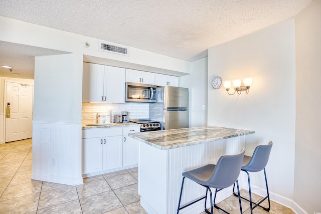 kitchen featuring sink, a kitchen breakfast bar, stainless steel appliances, light stone countertops, and white cabinets