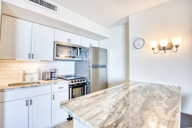 kitchen with appliances with stainless steel finishes, tasteful backsplash, sink, white cabinets, and light stone countertops