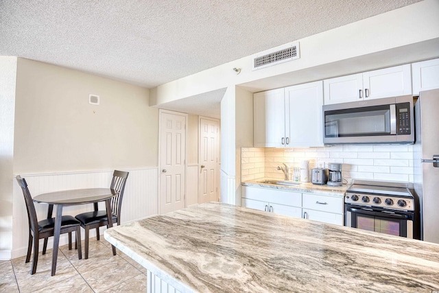 kitchen featuring white cabinetry, sink, stainless steel appliances, light stone countertops, and a textured ceiling