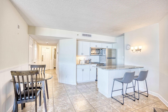 kitchen with appliances with stainless steel finishes, backsplash, a kitchen breakfast bar, light stone counters, and kitchen peninsula