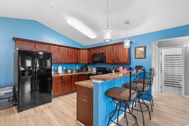 kitchen featuring lofted ceiling, light hardwood / wood-style flooring, a kitchen breakfast bar, pendant lighting, and black appliances