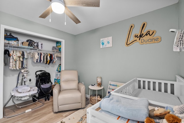 bedroom with a crib, wood-type flooring, a closet, and ceiling fan