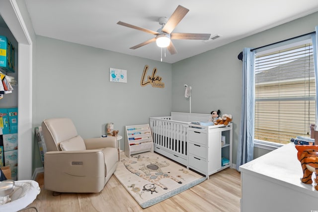 bedroom featuring a nursery area, ceiling fan, and light wood-type flooring