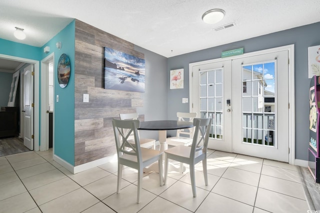 tiled dining area with wooden walls, french doors, and a textured ceiling