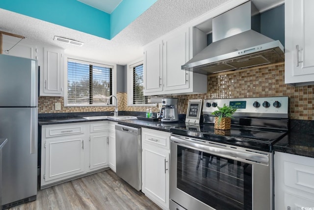 kitchen with sink, appliances with stainless steel finishes, light hardwood / wood-style floors, white cabinets, and wall chimney exhaust hood