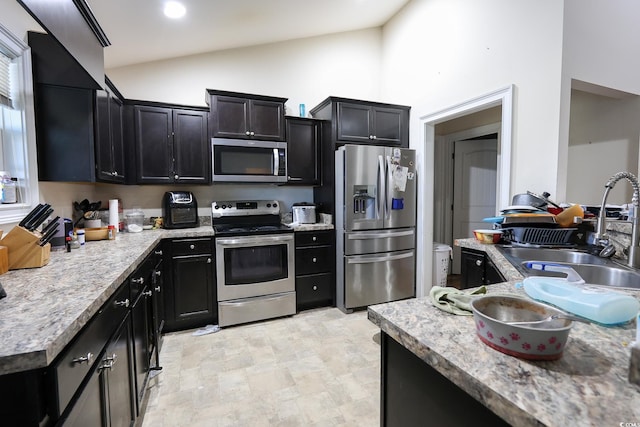 kitchen with high vaulted ceiling, dark cabinets, stainless steel appliances, a sink, and light countertops