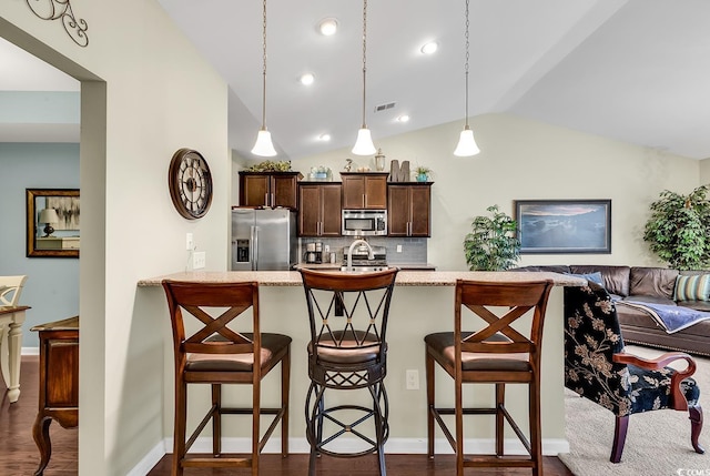 kitchen featuring pendant lighting, a breakfast bar, appliances with stainless steel finishes, dark brown cabinetry, and light stone countertops