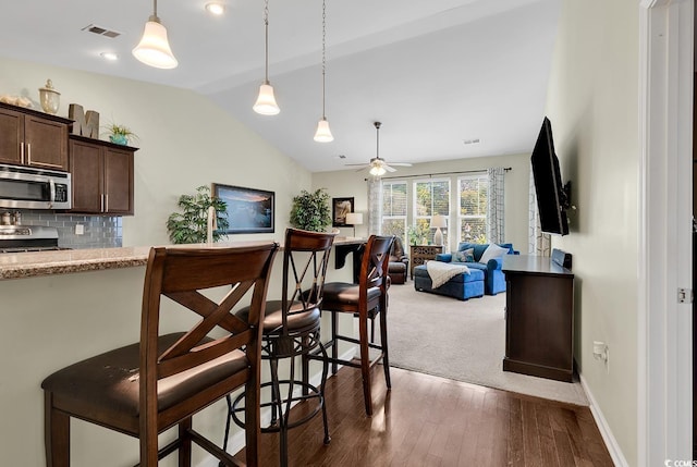 kitchen with a kitchen breakfast bar, vaulted ceiling, appliances with stainless steel finishes, and dark brown cabinetry