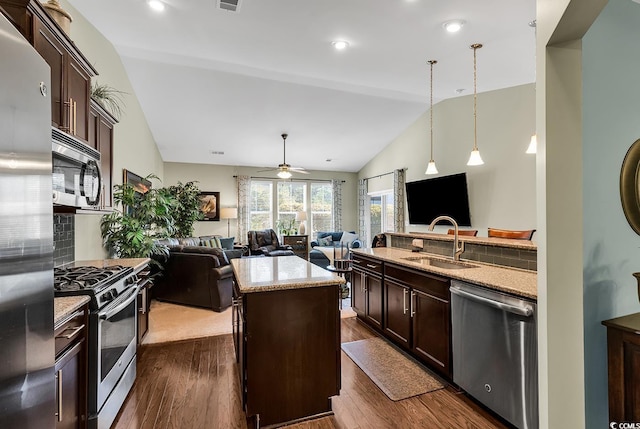 kitchen with sink, appliances with stainless steel finishes, hanging light fixtures, a center island, and light stone counters