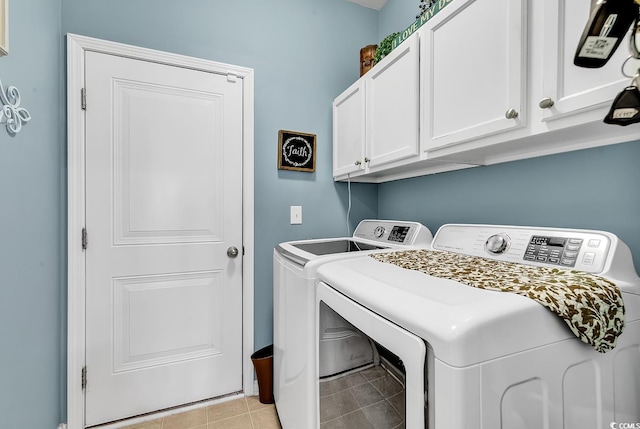 clothes washing area featuring cabinets, light tile patterned floors, and washer and clothes dryer