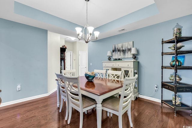 dining space with dark wood-type flooring, a tray ceiling, and a notable chandelier