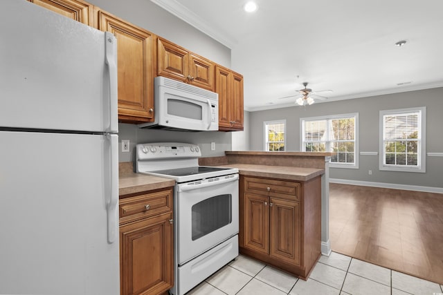 kitchen featuring brown cabinets, light tile patterned floors, ornamental molding, white appliances, and a peninsula