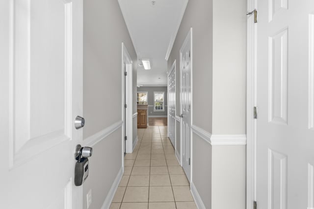 hall featuring baseboards, ornamental molding, and light tile patterned flooring