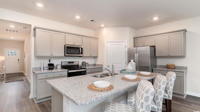 kitchen with sink, a breakfast bar area, stainless steel appliances, light stone countertops, and a center island with sink