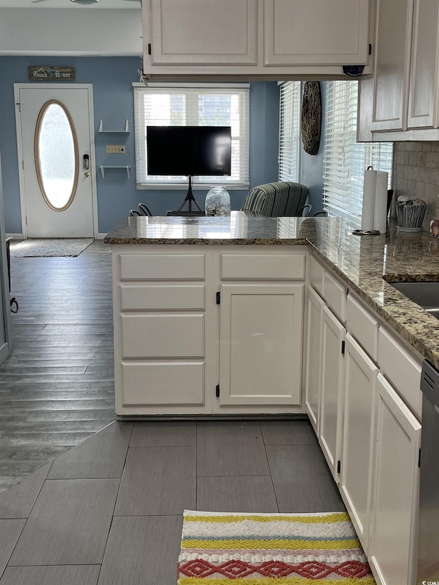 kitchen featuring white cabinets, decorative backsplash, stainless steel dishwasher, kitchen peninsula, and light stone countertops