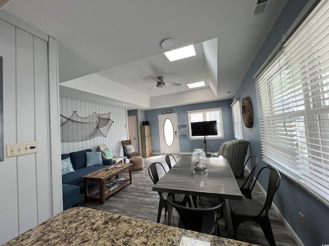 dining room featuring ceiling fan, a tray ceiling, a skylight, and dark wood-type flooring