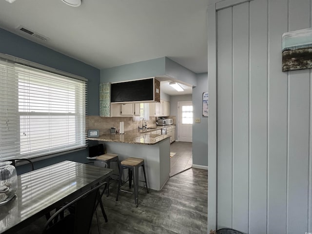 kitchen featuring a breakfast bar area, backsplash, dark hardwood / wood-style floors, light stone counters, and kitchen peninsula