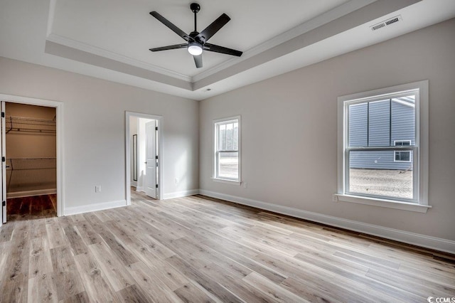 unfurnished bedroom featuring connected bathroom, crown molding, a spacious closet, a raised ceiling, and light hardwood / wood-style floors