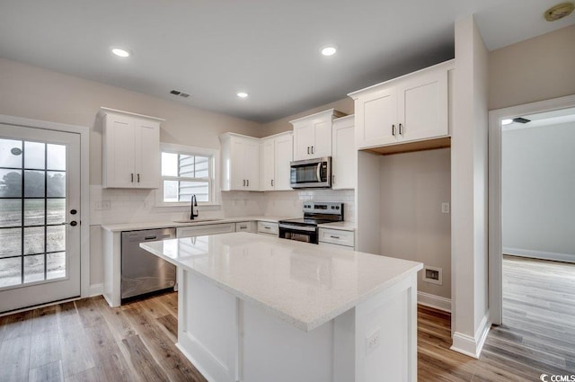 kitchen with sink, appliances with stainless steel finishes, tasteful backsplash, white cabinets, and a kitchen island