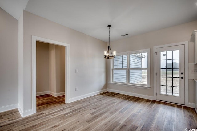 unfurnished dining area featuring an inviting chandelier and light hardwood / wood-style floors