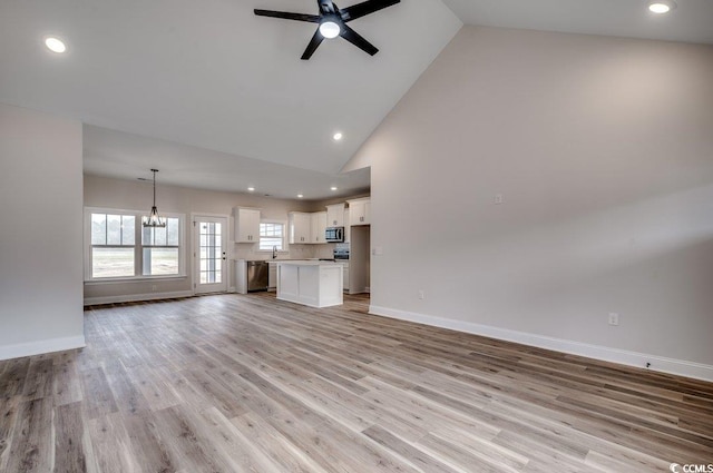 unfurnished living room with high vaulted ceiling, sink, ceiling fan with notable chandelier, and light hardwood / wood-style floors