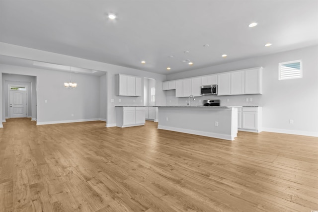 unfurnished living room featuring recessed lighting, baseboards, light wood-type flooring, and an inviting chandelier