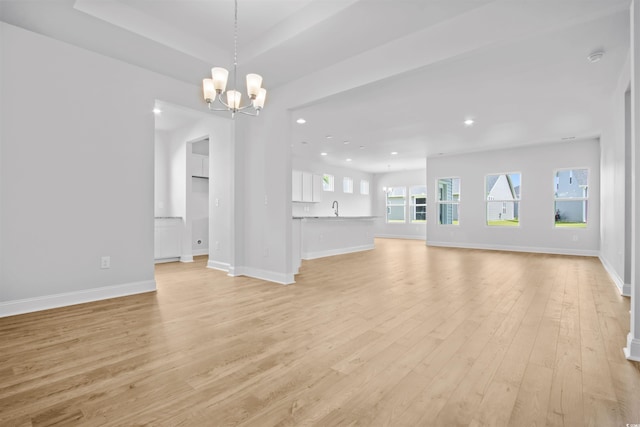 unfurnished living room featuring recessed lighting, baseboards, a notable chandelier, and light wood-style flooring