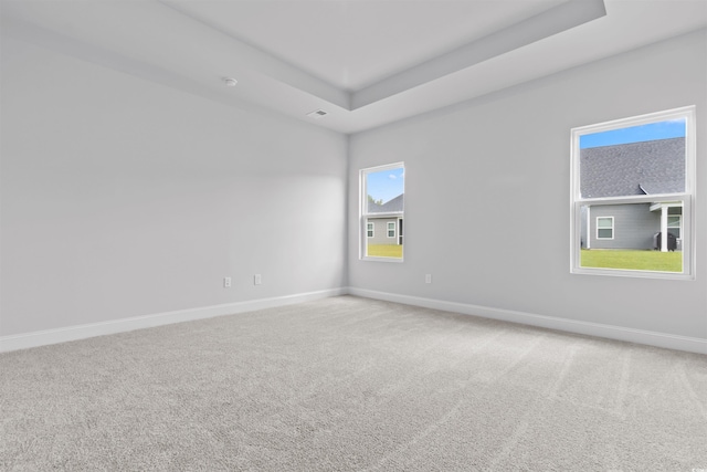 carpeted spare room featuring a tray ceiling and baseboards